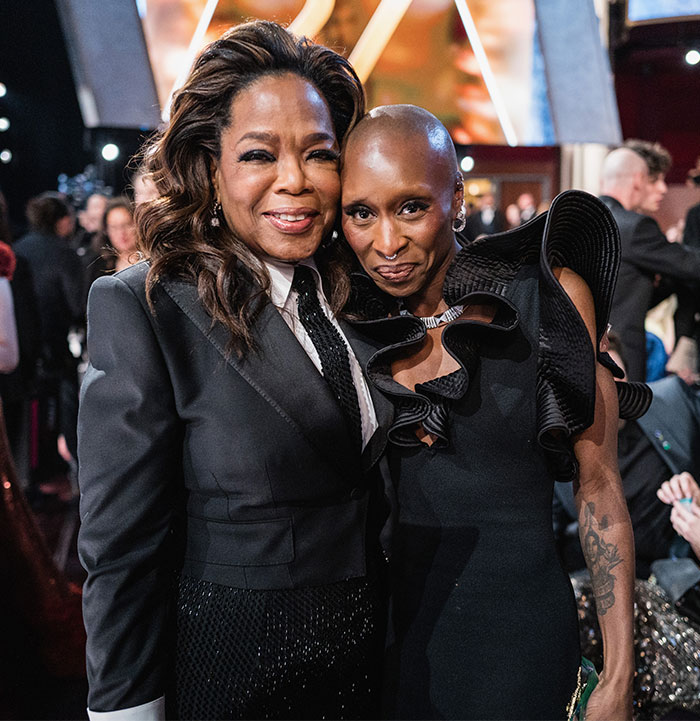 Two individuals smiling together in elegant attire, capturing a behind the scenes moment at the Oscars 2025.