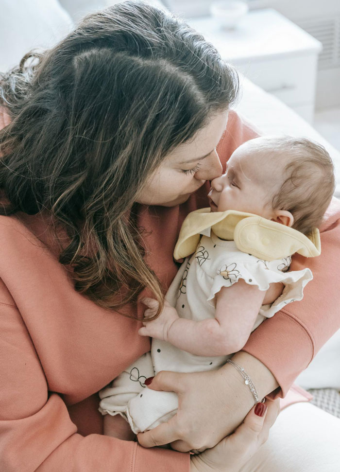 Mother cuddling a newborn battling pneumonia, both in soft pastel tones, showing tender care and concern.