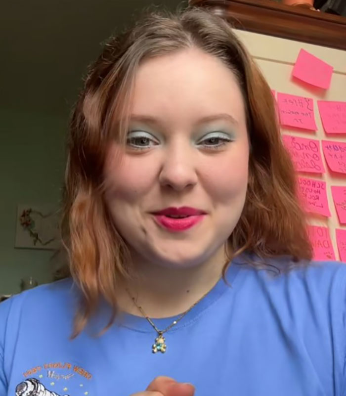 Young woman smiling in front of a wall with sticky notes, discussing her NASA astronaut father's health concerns.