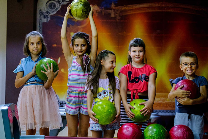 Children at a birthday party holding colorful bowling balls, smiling and posing together indoors.