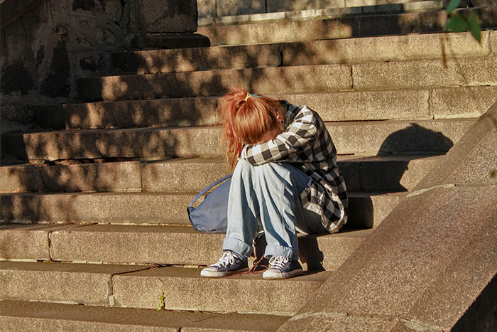 A young girl sitting alone on stone steps, wearing casual clothes, with her head down.