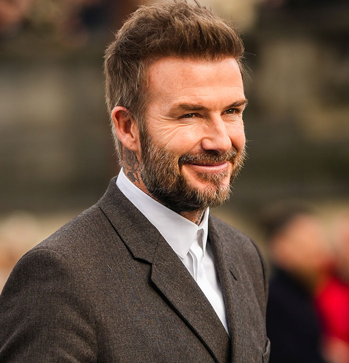 David Beckham smiling in a suit at an outdoor event, related to ex-assistant's affair interview.