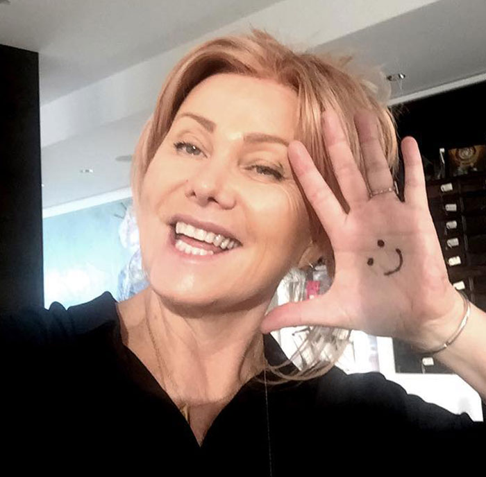 Smiling woman with a smiley face drawn on her hand; related to Hugh Jackman and Deborra-Lee Furness' divorce issues.