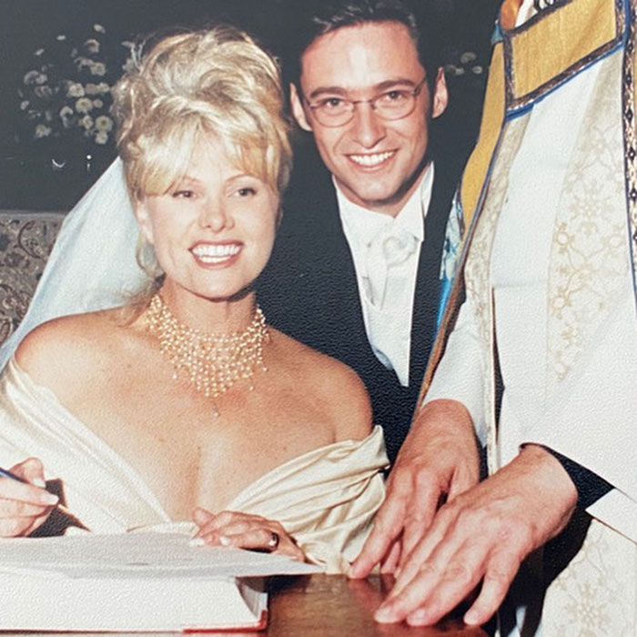 A bride and groom sitting together, smiling on their wedding day, as the bride signs a document.