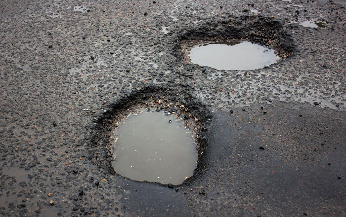 Potholes filled with water on asphalt, highlighting the need for new inventions in road maintenance.