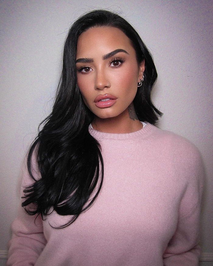 Woman in pink sweater showcasing weight loss transformation with long black hair against a plain background.