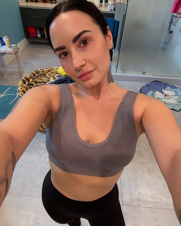 Demi Lovato showcases weight loss transformation in a gray top, standing in a stylish bathroom.
