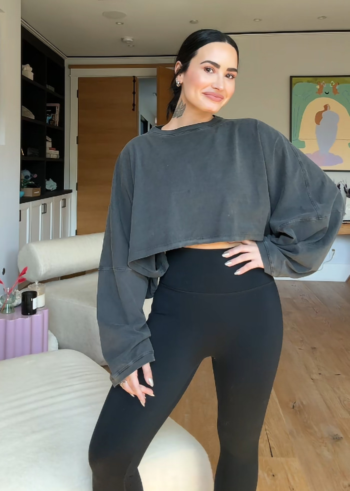 Demi Lovato shows weight loss transformation, wearing a loose-fitting sweatshirt and black leggings in a stylish room.