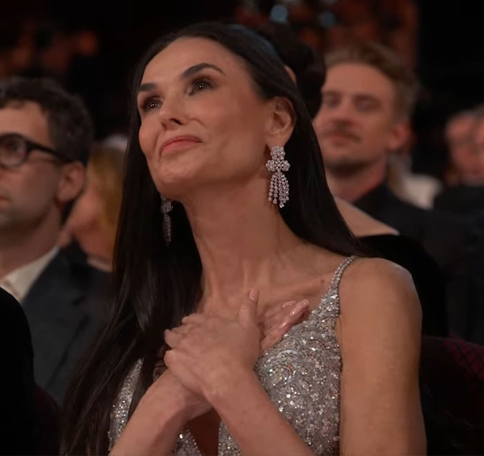 Demi Moore at the Oscars, hands on chest, showing emotion during a heartfelt moment.