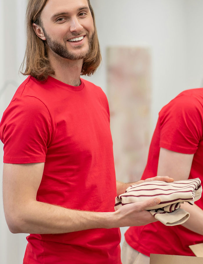 Man in a red shirt folding clothes, smiling, representing as a brand.