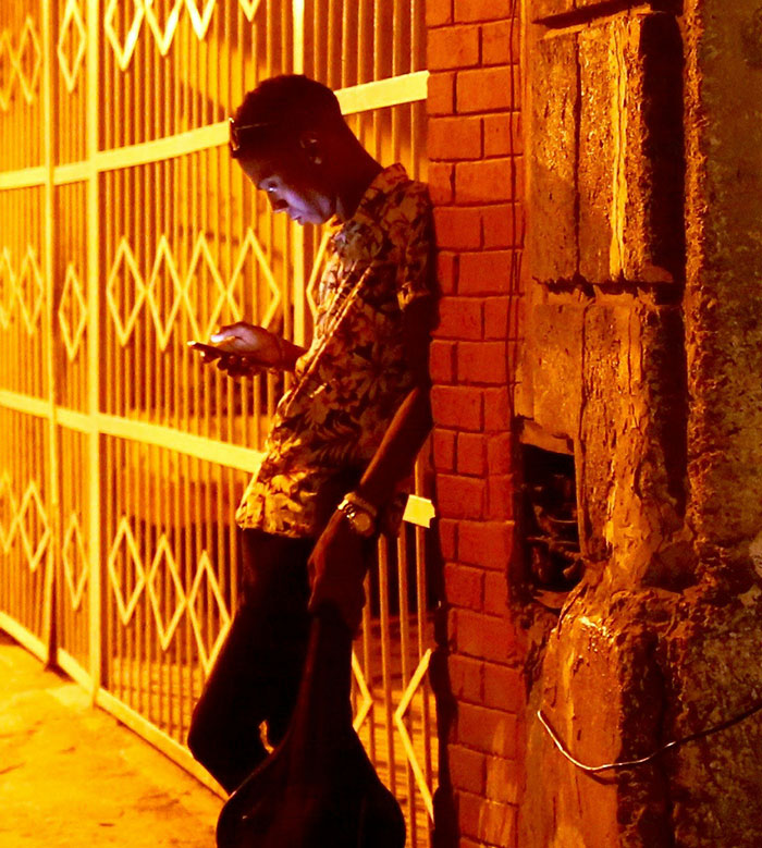 "Person in floral shirt checks phone under streetlight, embodying brand-like demeanor against urban backdrop."