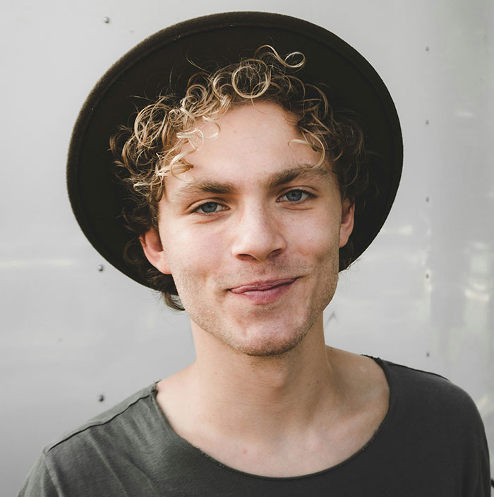 Smiling person wearing a black hat, representing a youthful brand style.