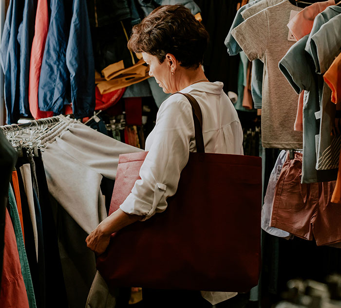 A woman shopping in a clothing store, examining items while carrying a large red bag.