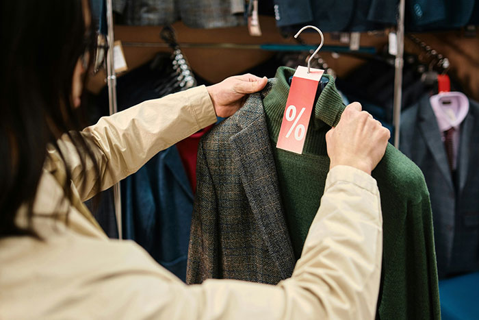 Person holding a green sweater with a discount tag, symbolizing ex-as-a-brand concept in a clothing store.