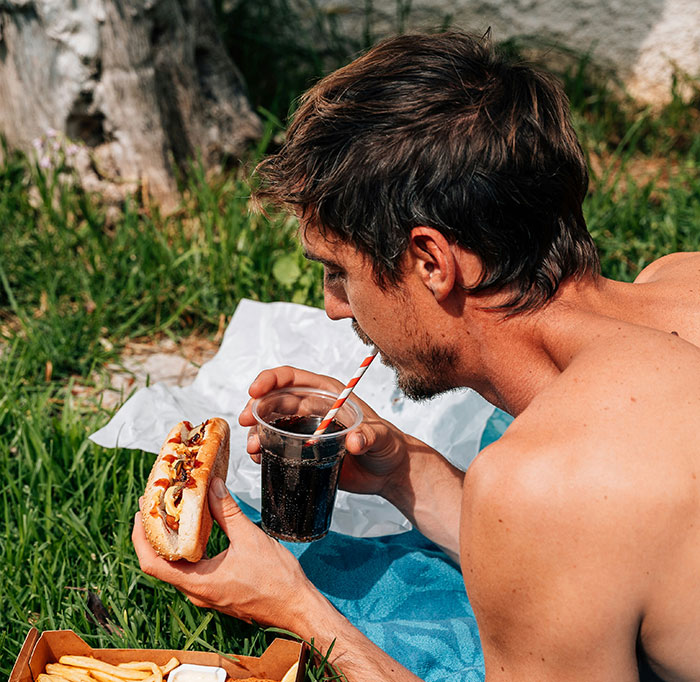 A man enjoying a picnic, holding a hot dog and a soda, representing a brand-like experience.