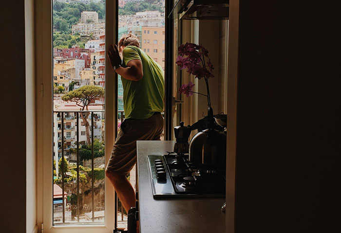 Man in a green shirt on a balcony, overlooking a colorful hillside town, embodying the concept of "ex as a brand."
