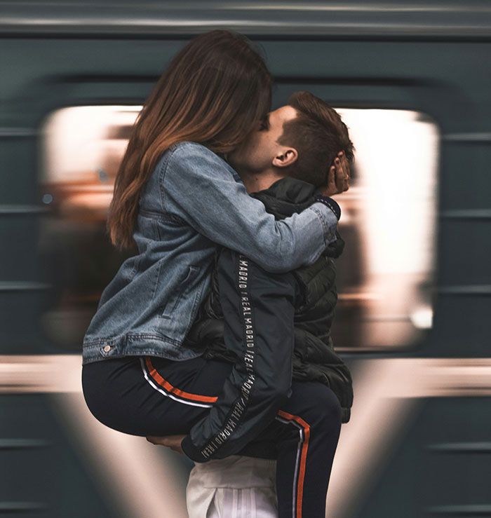 A couple embracing passionately in front of a moving subway train, capturing a candid romantic moment.