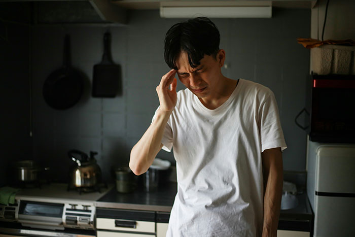 Man in a kitchen holding his head, expressing stress while contemplating his ex as a brand.