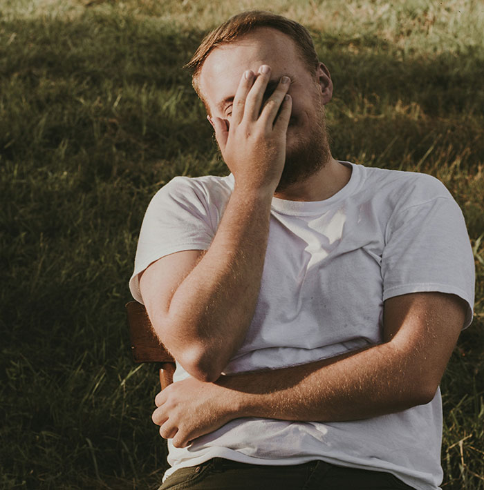A person in a white shirt sitting on grass, covering their face, conveying an ex as a brand sentiment.