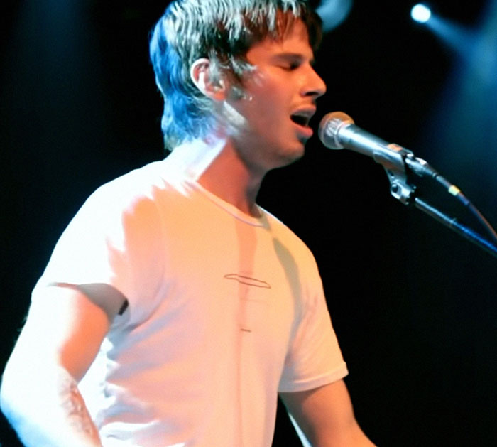 Musician singing passionately on stage, wearing a white shirt. Wholesome appearance hides a disturbing backstory.