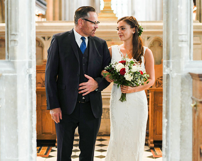Man in suit walking with bride holding flowers, scene appearing wholesome.