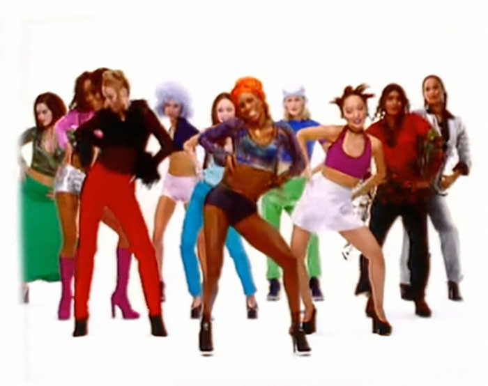 A group of people in colorful outfits dancing energetically, conveying a wholesome vibe with diverse backstories.