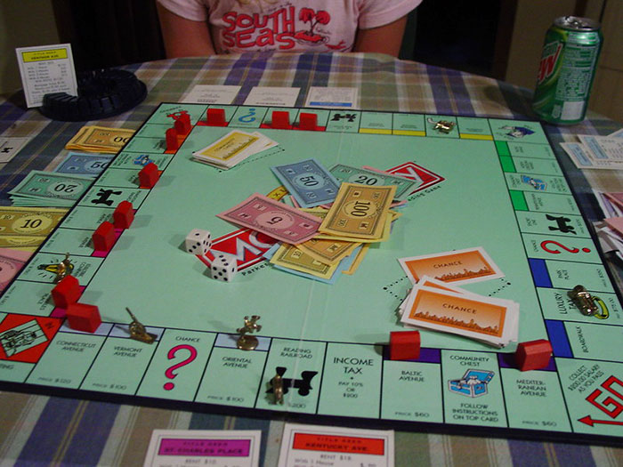 Monopoly board game on a table with colorful money and houses, hinting at wholesome elements with potentially disturbing backstories.