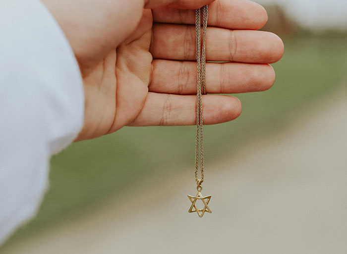 Hand holding a necklace with a Star of David pendant, symbolizing unexpected family secrets from an online DNA test.