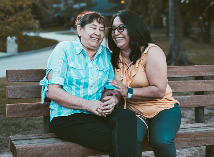 Two women sitting on a park bench, laughing, enjoying a moment, symbolizing unexpected family secrets from DNA tests.