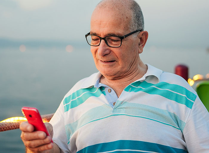 Elderly man with glasses smiling at a smartphone, possibly reading DNA test results.
