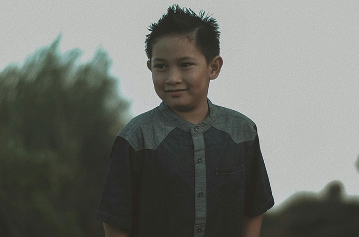 Young boy outdoors in dim light, wearing a two-toned shirt, representing unexpected family secrets.