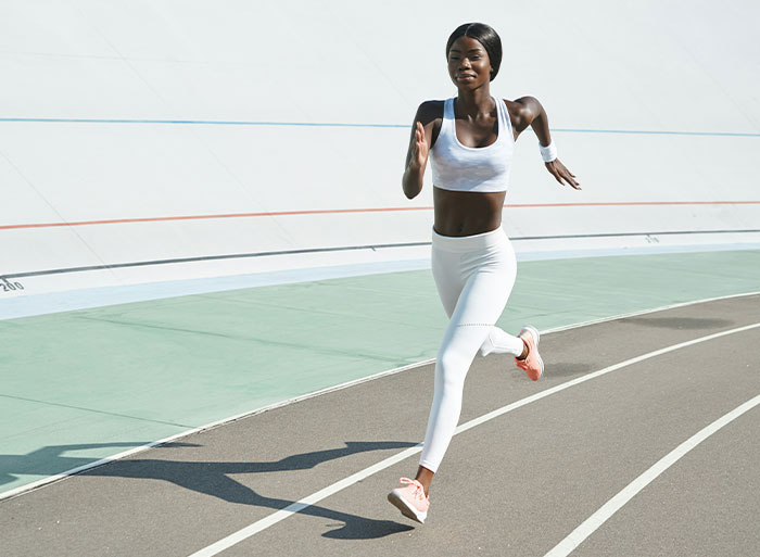 Woman jogging on an outdoor track wearing white activewear, under a clear sky.