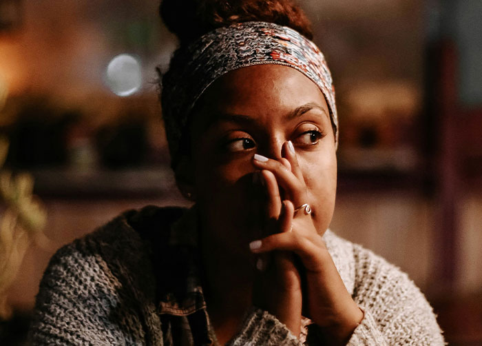Woman looking thoughtful, wearing a headband and sweater, with hands clasped near her face, pondering about a vanished man.