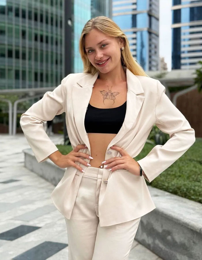 Model in a light suit smiling in a Dubai urban setting.