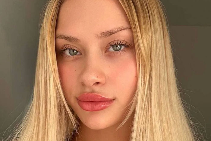 Blonde model with blue eyes, looking directly at the camera, neutral expression.