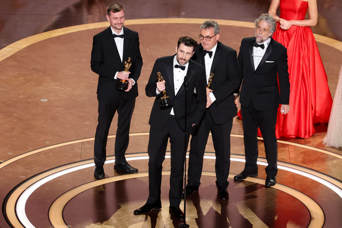 Oscar winners 2025 on stage, holding awards, wearing tuxedos at the ceremony.