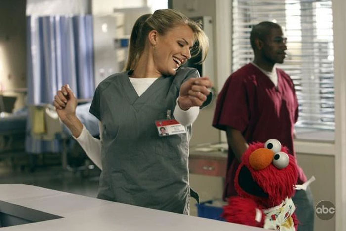 Scrubs star dancing with Elmo, wearing scrubs in a lively hospital setting.