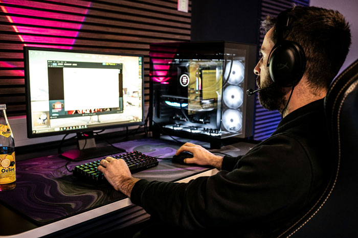 Man wearing headset using computer, dimly lit gaming setup, gaslighting theme.