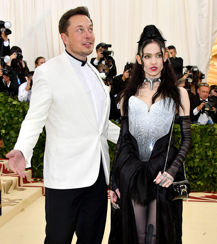 Elon Musk and Grimes pose at a public event, surrounded by photographers, amid privacy debate.