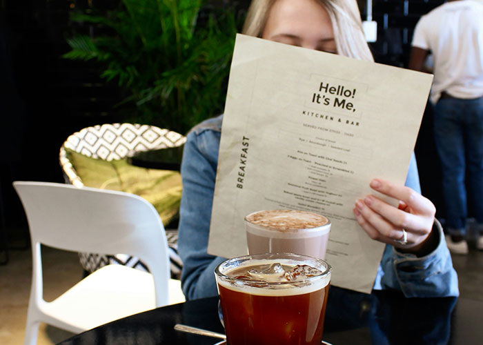 Woman at cafe holding menu, drinks on table, highlighting her dislike for boyfriend's restaurant behavior.