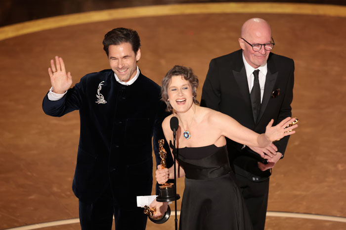 People celebrating on stage at the Oscars 2025, holding an award and waving to the audience.