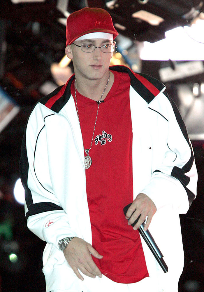 Eminem in a white jacket and red shirt holding a microphone, exemplifying net worth success.