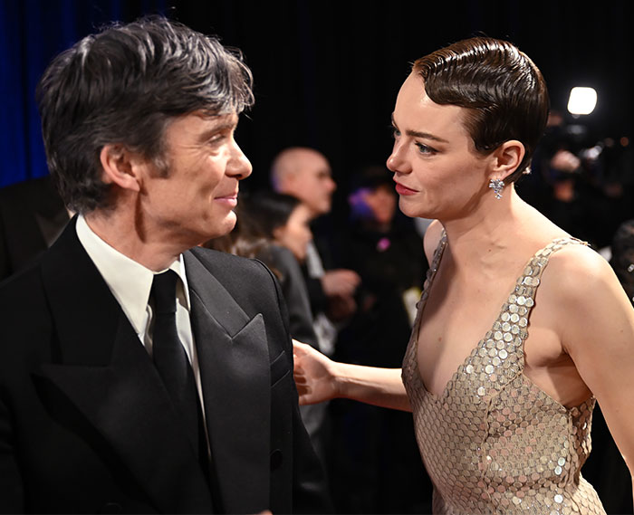 Two individuals sharing a candid moment backstage at Oscars 2025, dressed in formal attire.