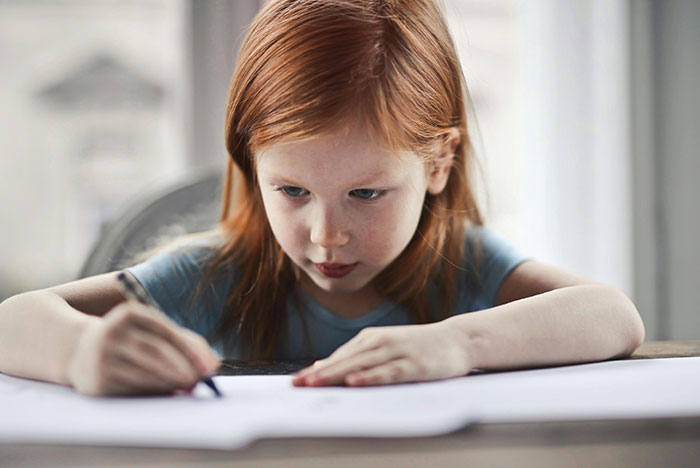 Young girl with red hair, focused on drawing with a pencil, linked to university funds and past behavior story.