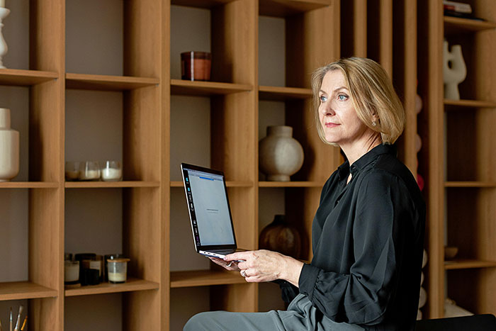 Woman holding a laptop in a modern office, shelves in background, expressing concern over university funds issue.