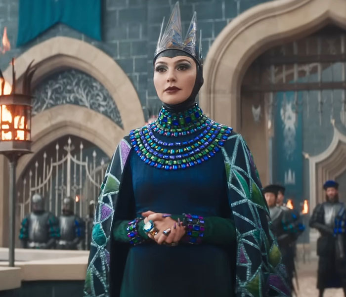 Actress in regal attire from 'Snow White' film scene, set in a castle with guards in the background.