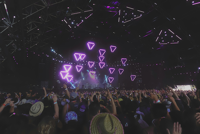 Concert crowd under a canopy of neon lights and geometric patterns.