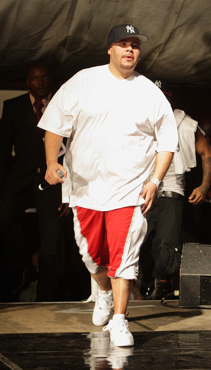 Man in oversized white shirt and red shorts walking on stage, holding a microphone; raising questions about beauty standards. Man in oversized white shirt and red shorts walking on stage, holding a microphone; raising questions about beauty standards.