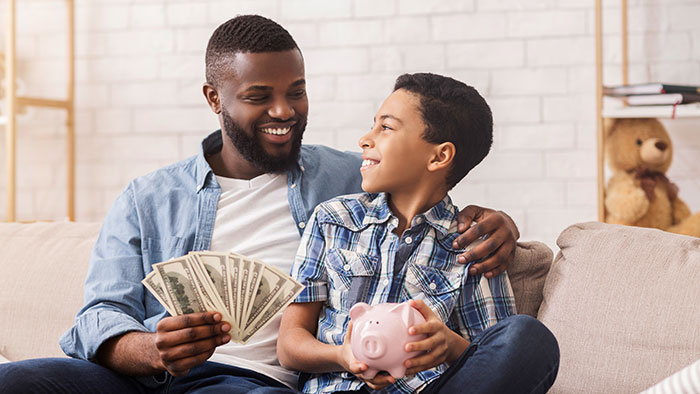 Man smiling, holding cash with son holding a piggy bank, discussing rent and earnings.