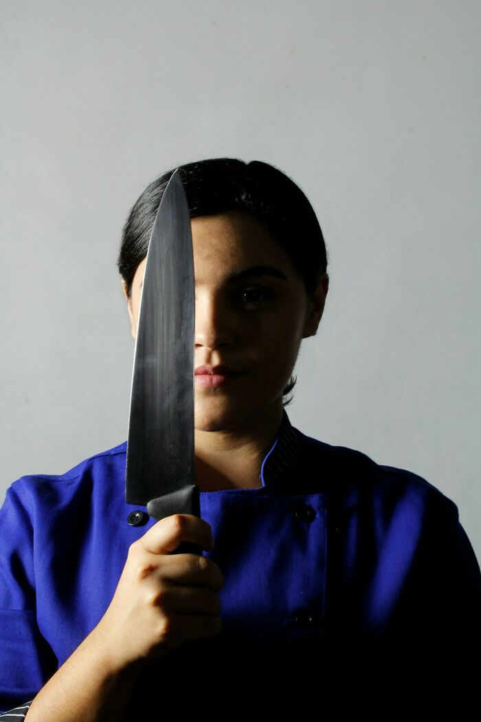 A person in a blue uniform holding a large knife vertically in front of their face, depicting strange object removal themes.